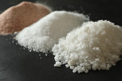 Photo of Different types of organic salt on black table, closeup