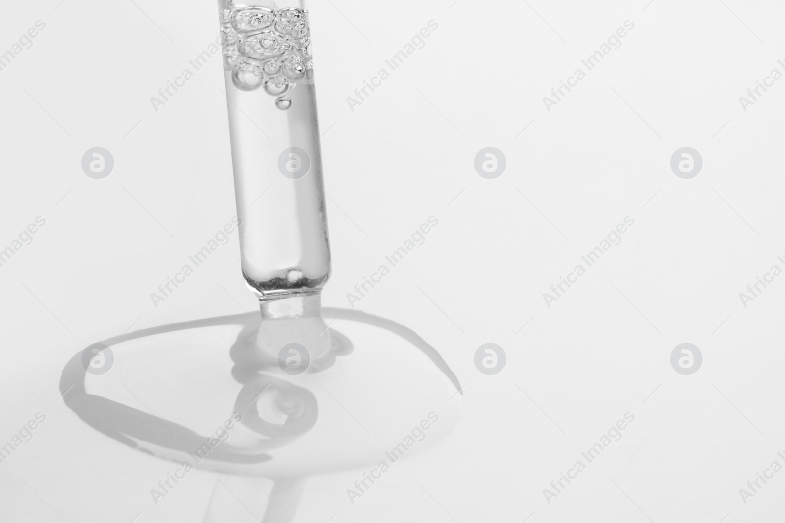 Photo of Dripping face serum from pipette on white background, closeup. Space for text