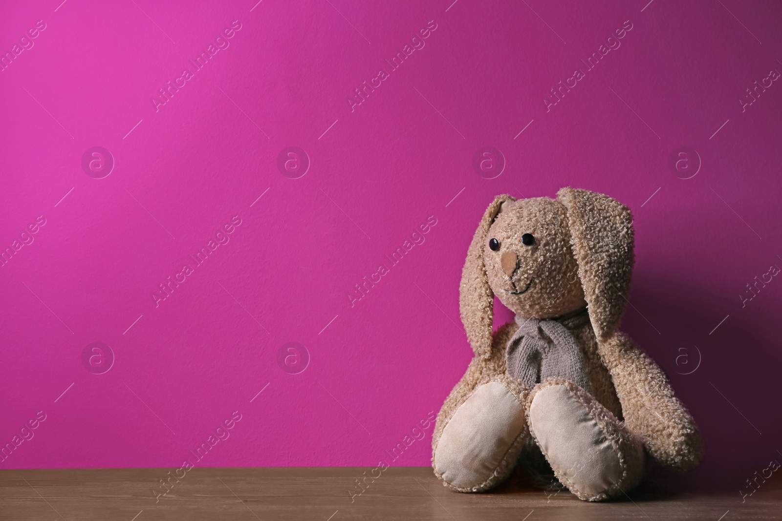 Photo of Abandoned toy bunny on table against color background. Time to visit child psychologist