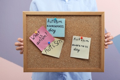 Woman holding board with phrases about autism on color background