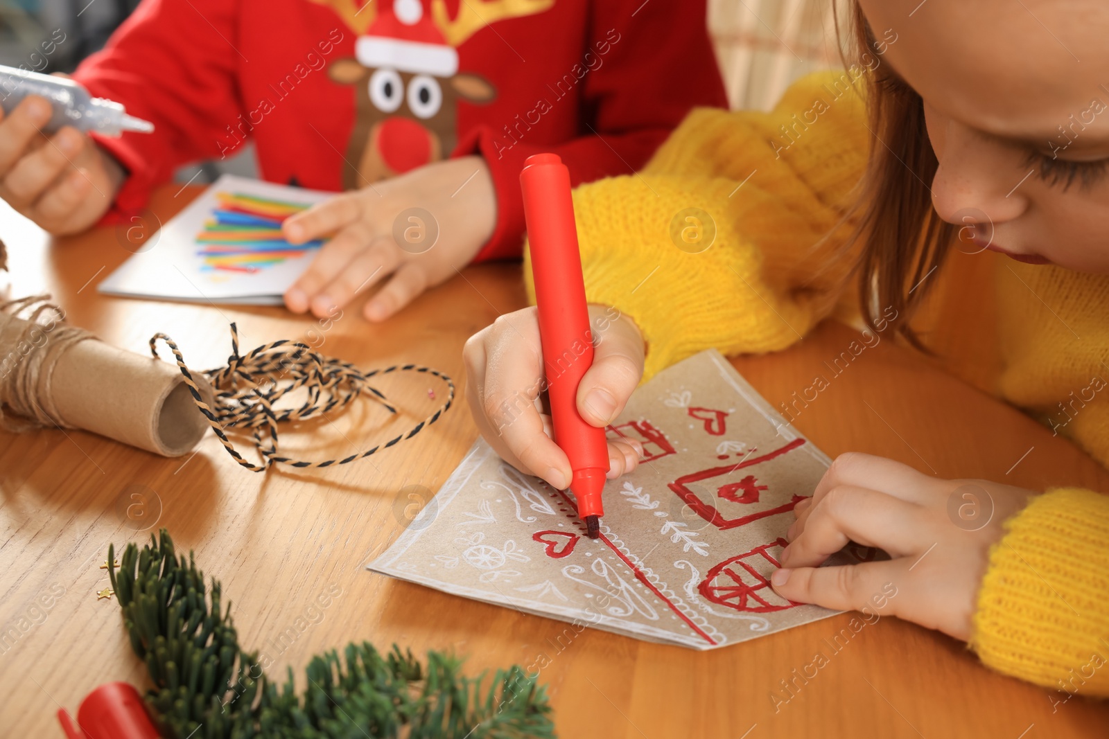 Photo of Cute little child making beautiful Christmas greeting card at wooden table, closeup