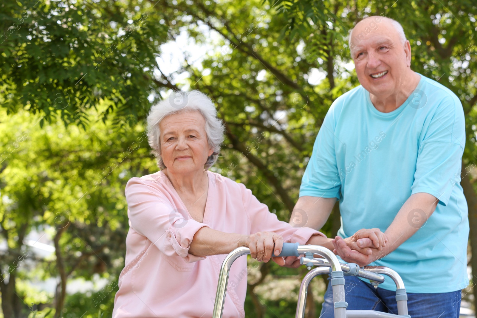 Photo of Elderly man helping his wife with walking frame outdoors