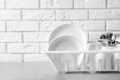Photo of Dish drainer with clean plates on table near brick wall. Space for text