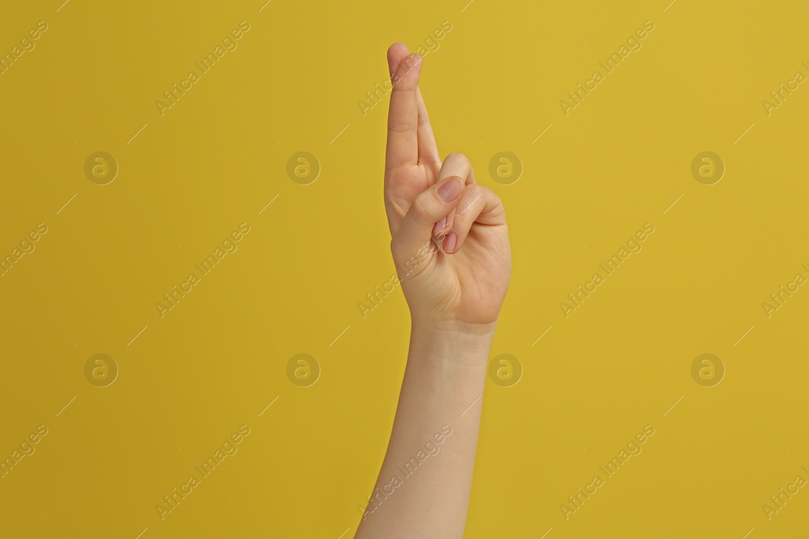 Photo of Woman showing crossed fingers on yellow background, closeup