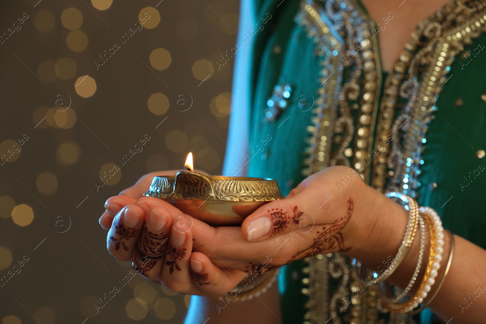 Photo of Woman holding lit diya lamp on brown background with blurred lights closeup view. Diwali holiday