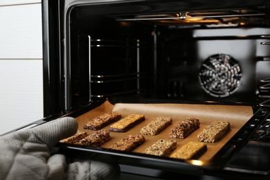 Photo of Woman taking delicious healthy granola bars from oven, closeup