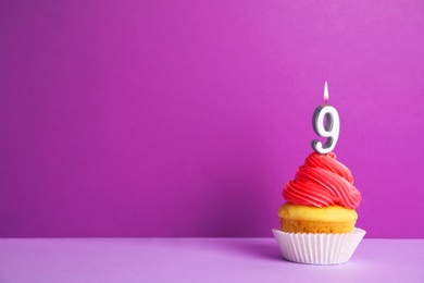 Photo of Birthday cupcake with number nine candle on violet background, space for text