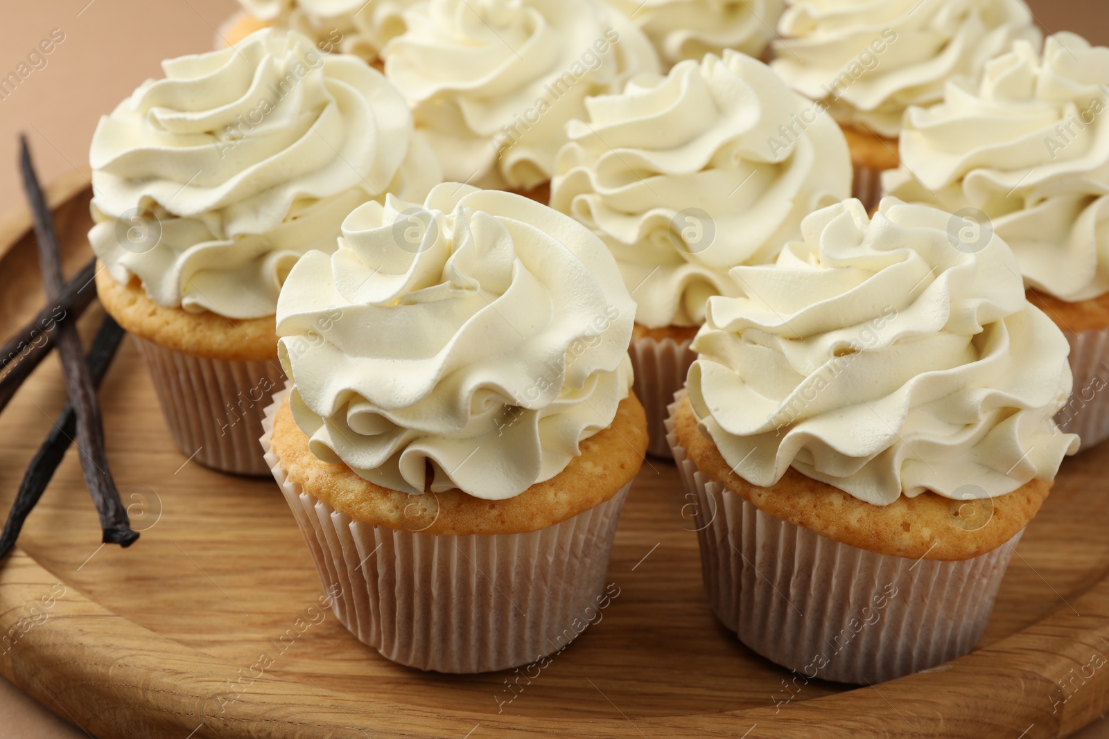 Photo of Tasty cupcakes with cream and vanilla pods on beige table, closeup