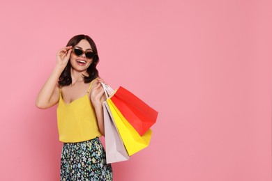 Photo of Beautiful young woman with paper shopping bags on pink background. Space for text
