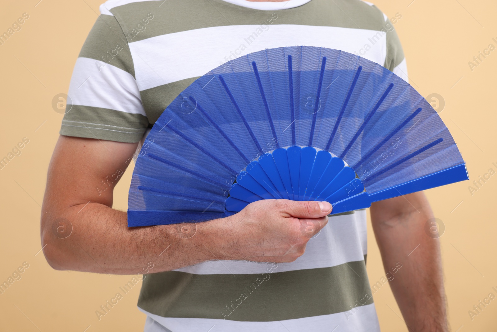 Photo of Man holding hand fan on beige background, closeup