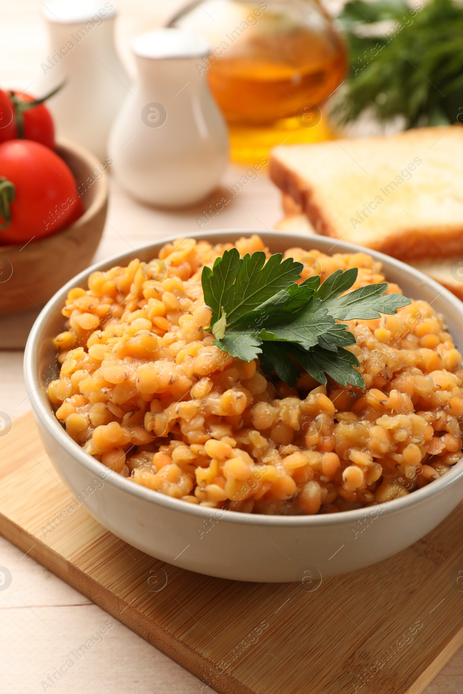 Photo of Delicious red lentils with parsley in bowl served on table, closeup