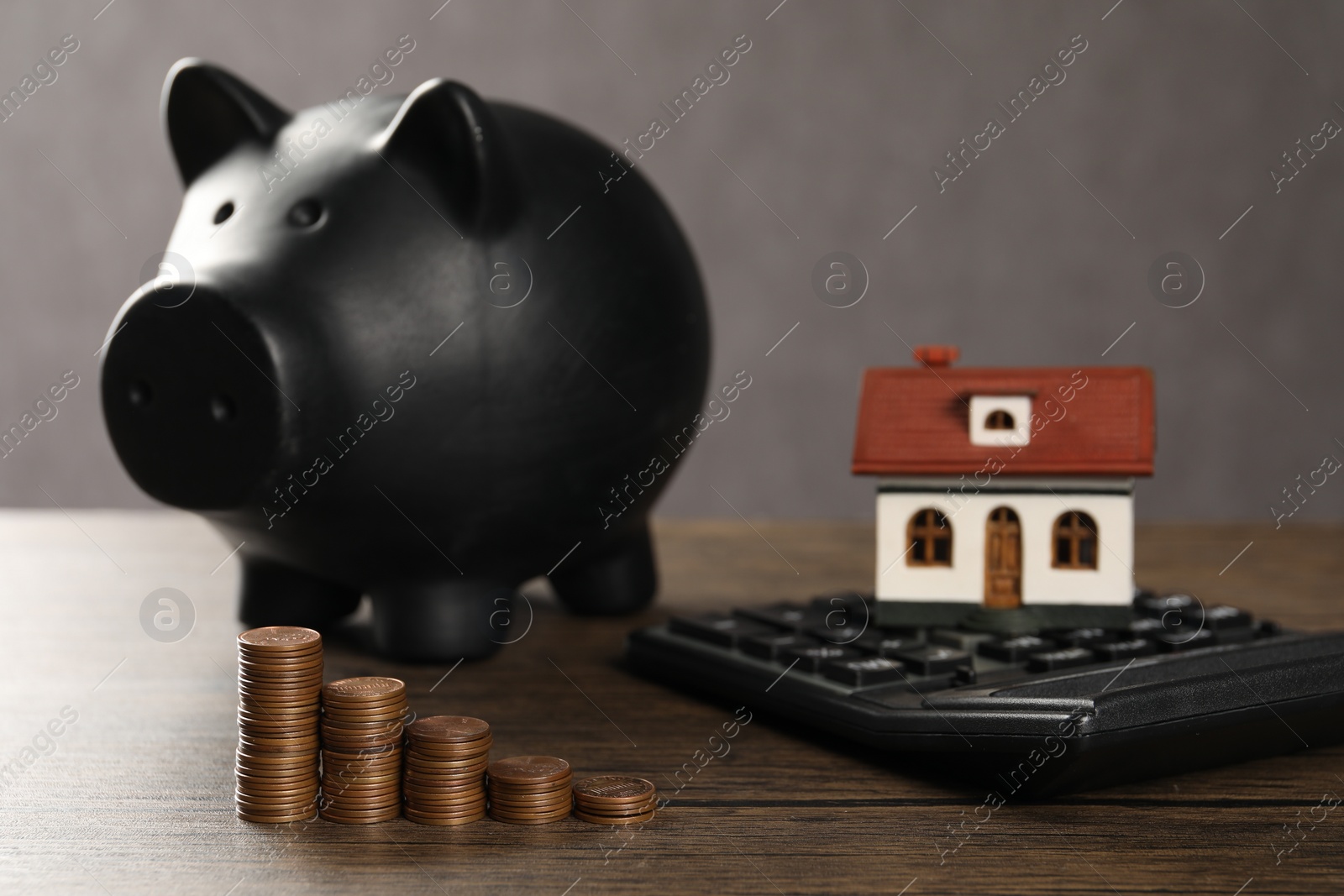 Photo of House model, piggy bank, calculator and stacked coins on wooden table, selective focus