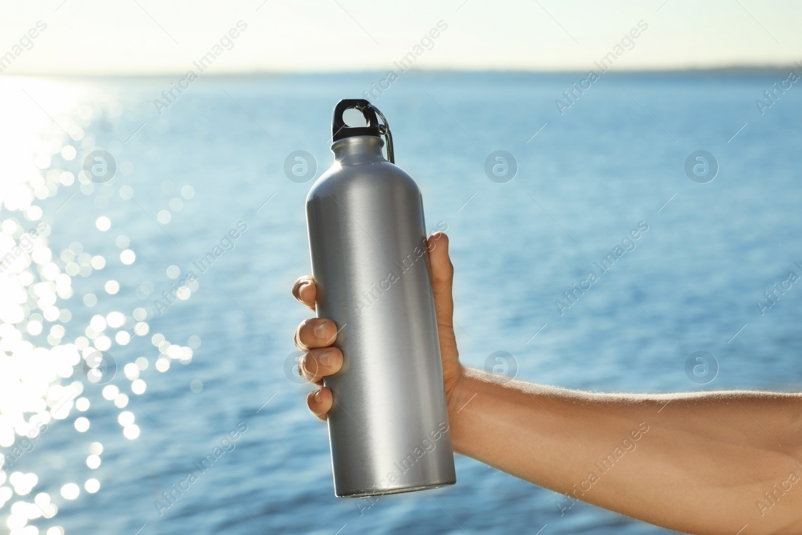 Photo of Young sporty man holding water bottle near river on sunny day