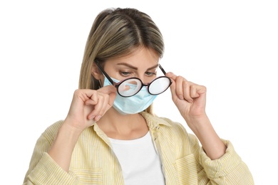 Photo of Woman wiping foggy glasses caused by wearing disposable mask on white background. Protective measure during coronavirus pandemic
