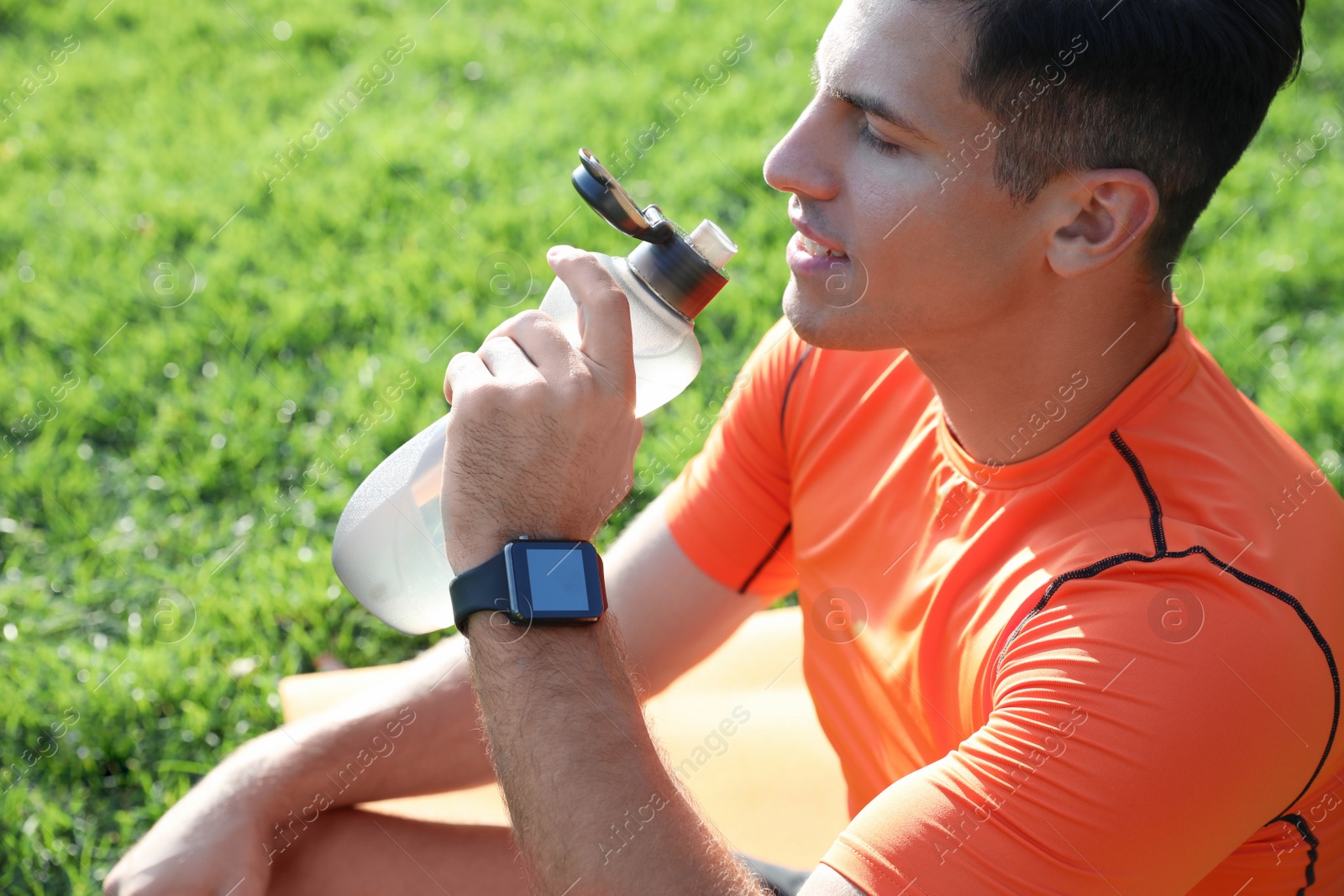 Photo of Man with fitness tracker drinking water after training in park, closeup