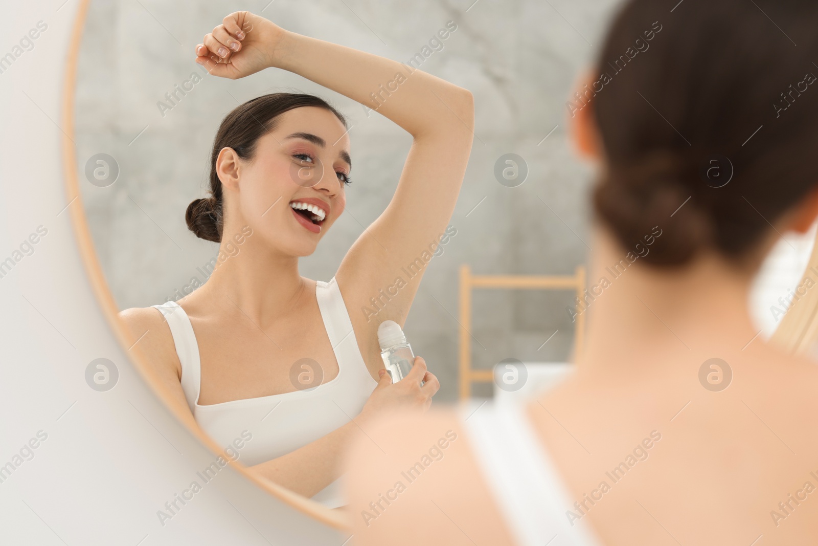 Photo of Beautiful woman applying deodorant near mirror in bathroom