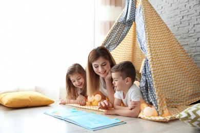 Photo of Nanny and little children reading book in tent at home