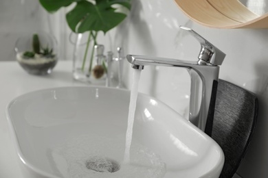 Photo of Sink with running water in modern bathroom