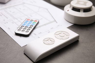 Photo of Remote controls, smoke detector and building plan on grey table, closeup. Home security system