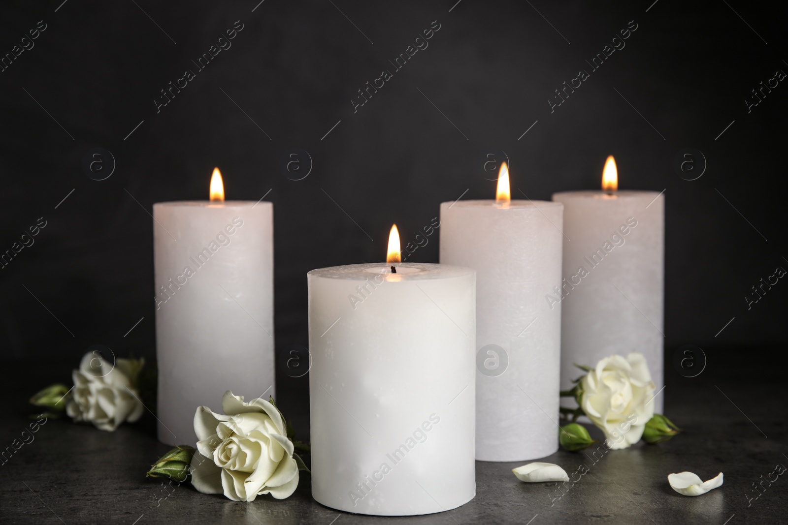 Photo of Burning candles and beautiful flowers on grey table