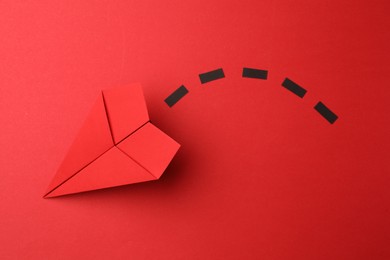 Photo of Handmade paper plane with dotted lines on red background, top view