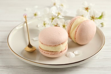 Photo of Delicious pink macarons and flowers on white wooden table, closeup
