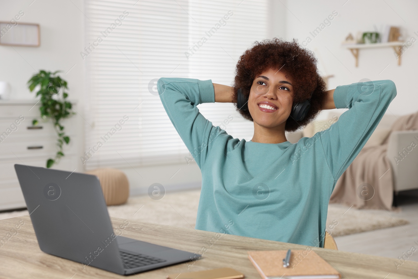 Photo of Young woman in headphones using laptop at wooden desk in room