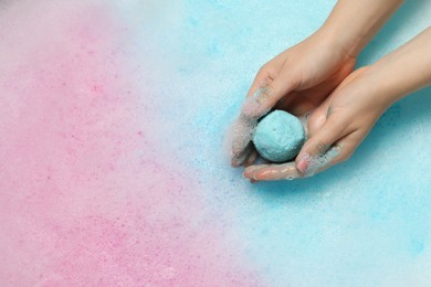 Photo of Woman holding bath bomb over water with foam, top view. Space for text