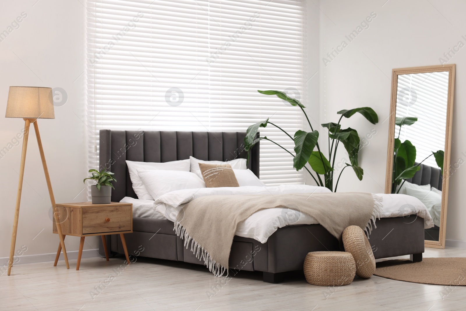 Photo of Stylish bedroom interior with large bed, lamp and houseplants