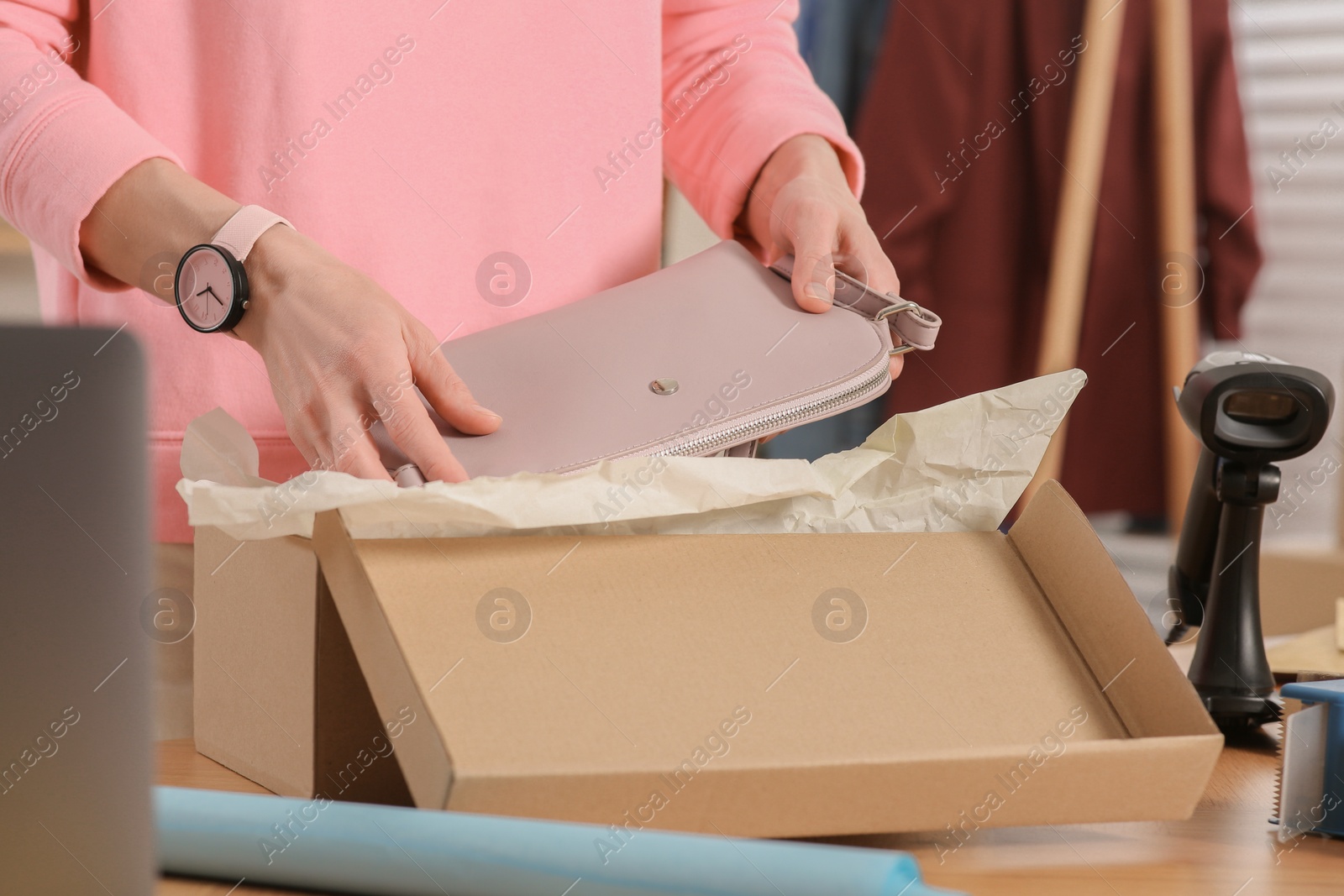 Photo of Seller packing bag into cardboard box at table in office, closeup. Online store