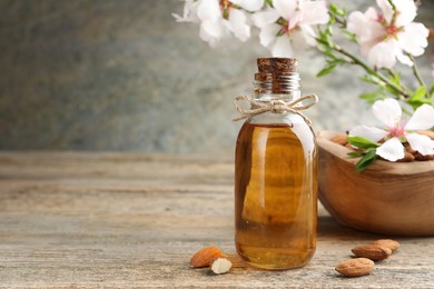 Photo of Almond oil in bottle, flowers and nuts on wooden table, closeup. Space for text