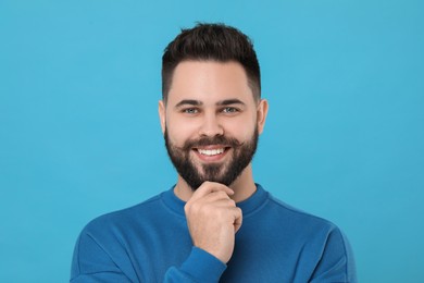 Portrait of happy young man with mustache on light blue background