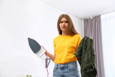 Emotional woman with iron and clothes at home