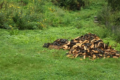 Photo of Pile of cut firewood on fresh green grass outdoors, space for text