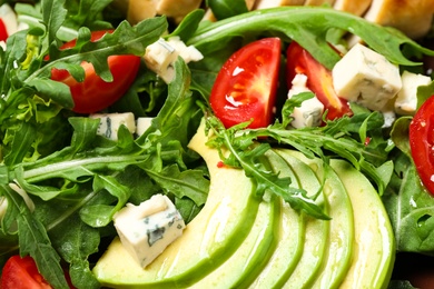 Photo of Delicious salad with arugula, tomatoes and avocado as background, top view