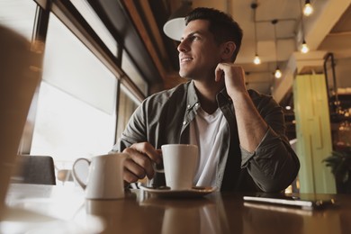 Photo of Handsome man with cup of coffee at cafe in morning