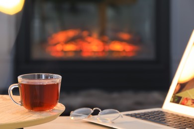 Photo of Glass cup of hot tea on wooden table near fireplace at home, space for text. Cozy atmosphere