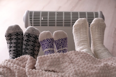 Photo of Family warming feet near electric heater at home, closeup