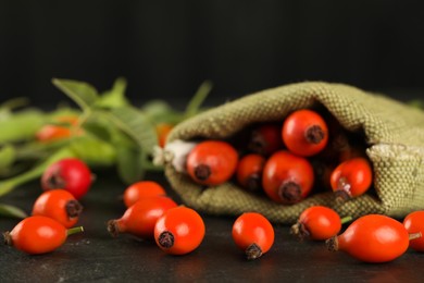 Photo of Ripe rose hip berries with green leaves on black table, closeup