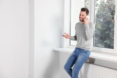 Man talking on phone near window indoors, space for text