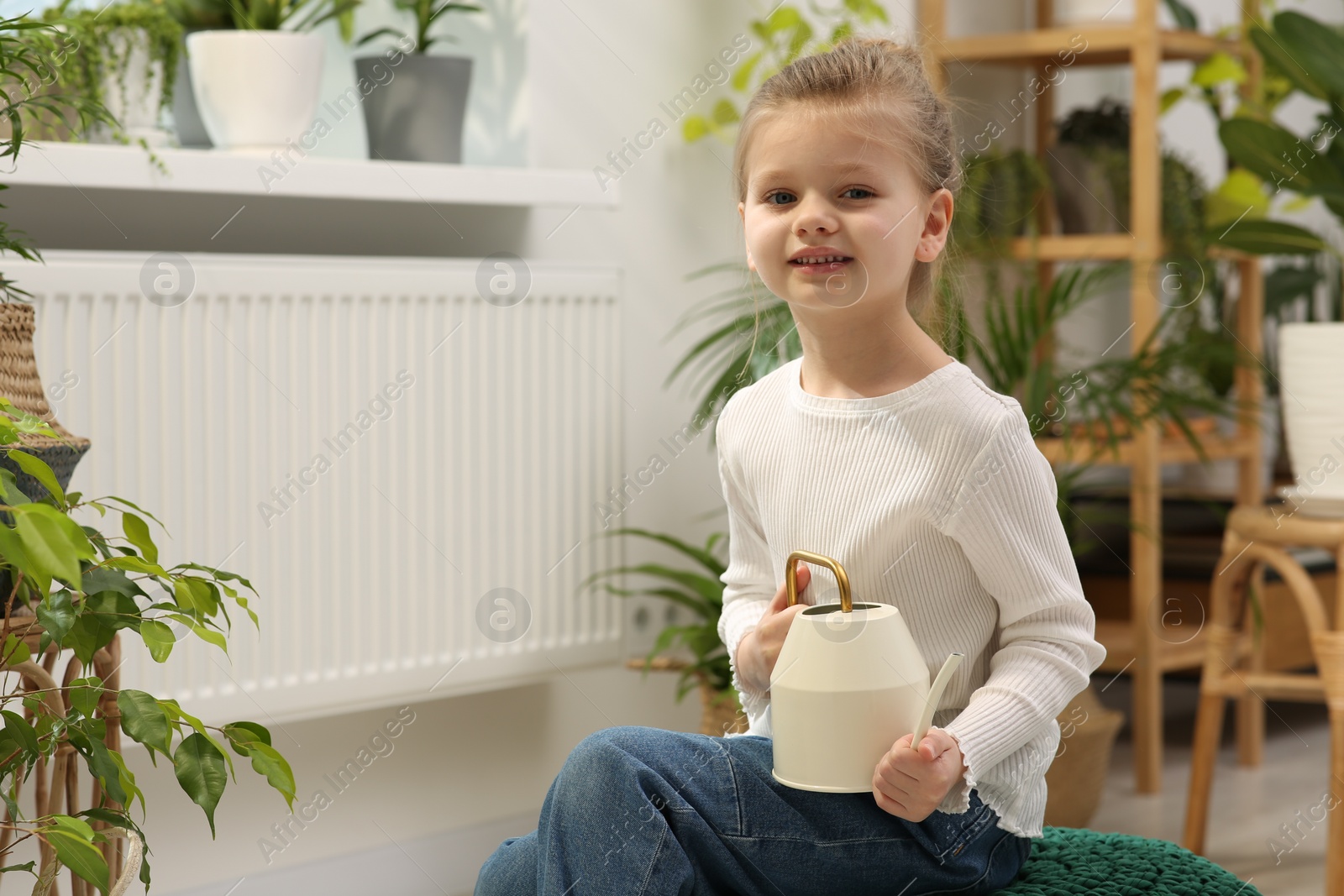 Photo of Cute little girl holding watering can near beautiful green plant at home. House decor