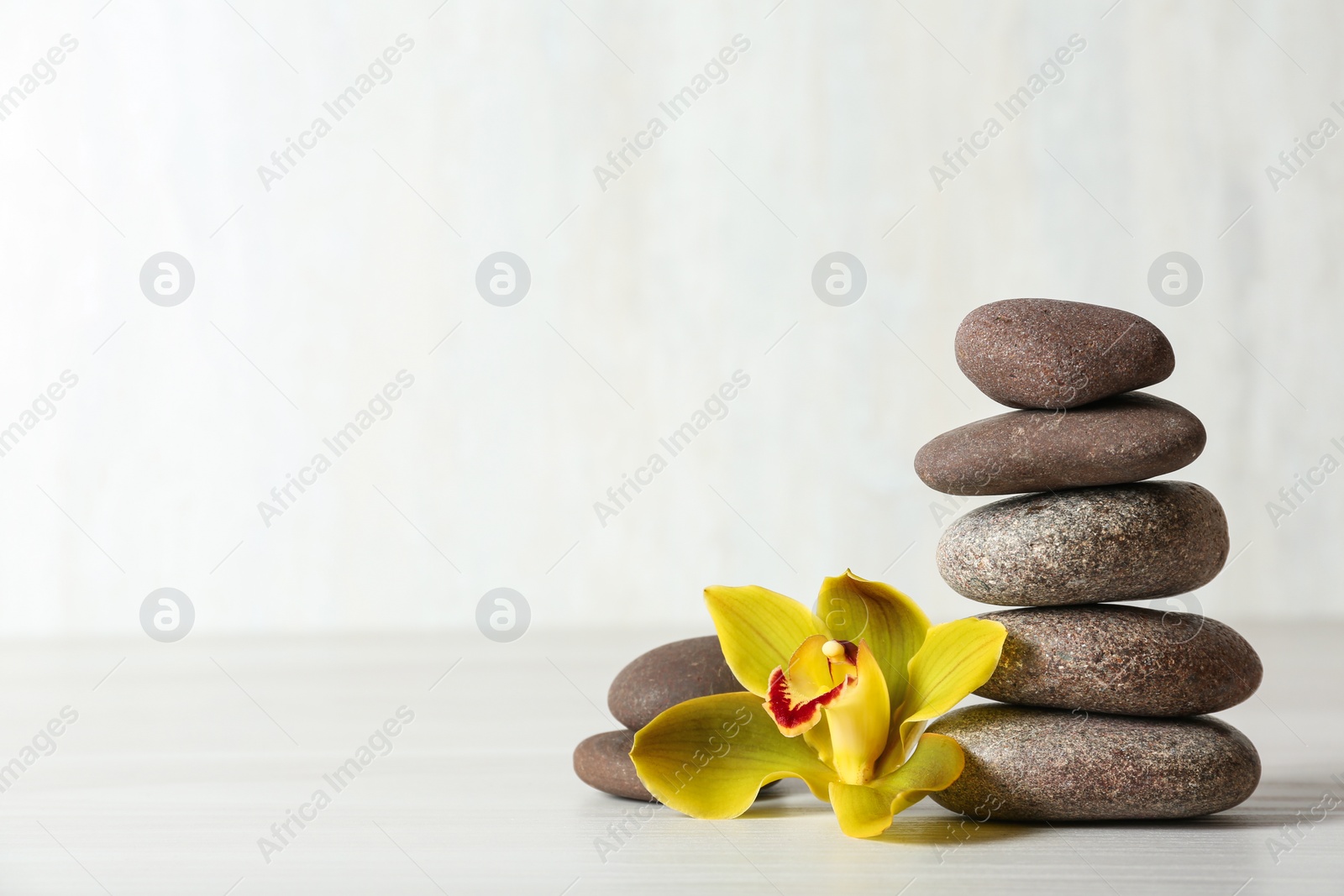 Photo of Stack of spa stones and flower on table against white background, space for text