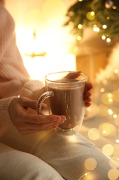 Photo of Woman with cup of drink and blurred Christmas lights on background, closeup
