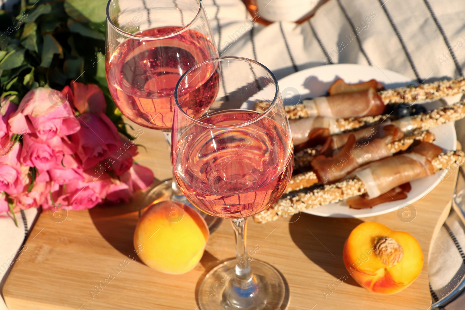 Photo of Glasses of delicious rose wine, flowers and food on white picnic blanket, closeup