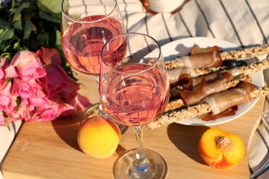 Photo of Glasses of delicious rose wine, flowers and food on white picnic blanket, closeup