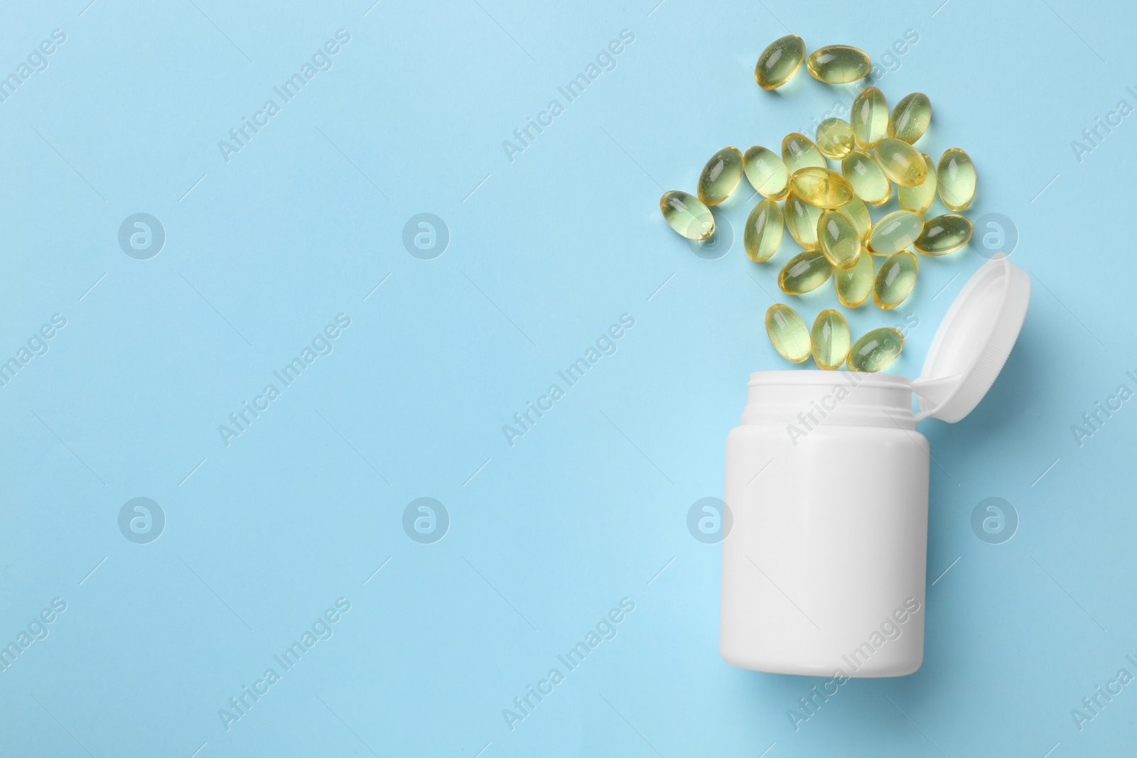 Photo of Vitamin capsules and bottle on light blue background, top view. Space for text