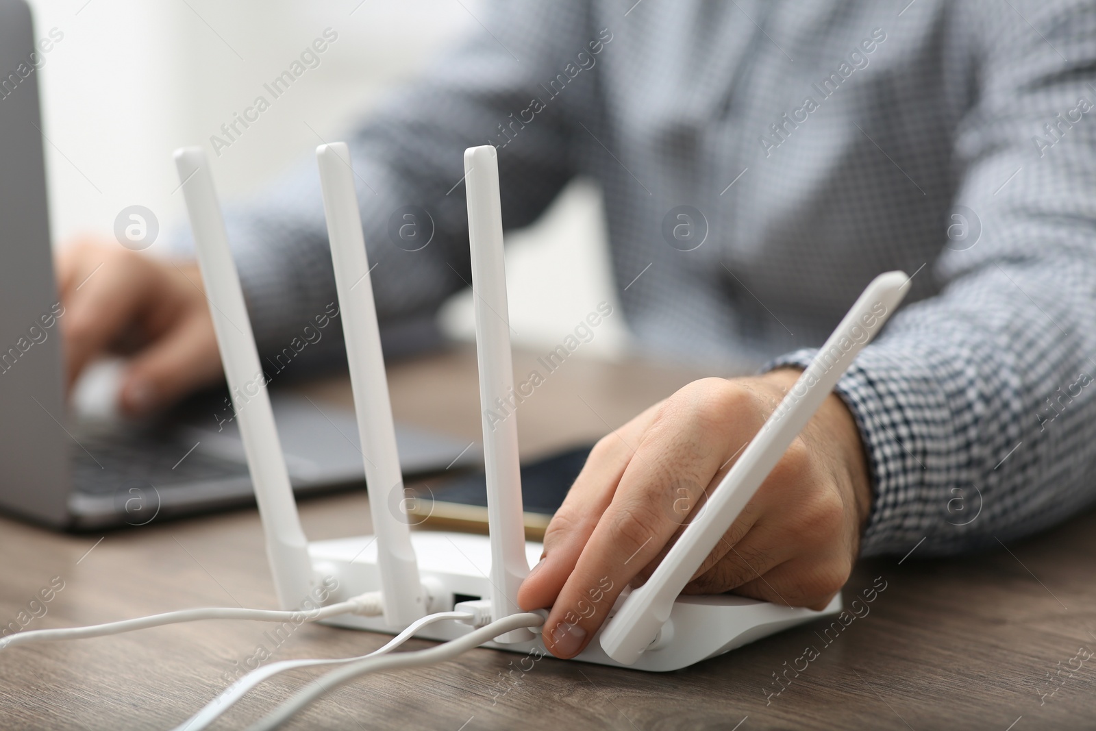 Photo of Man inserting cable into Wi-Fi router at wooden table indoors, closeup