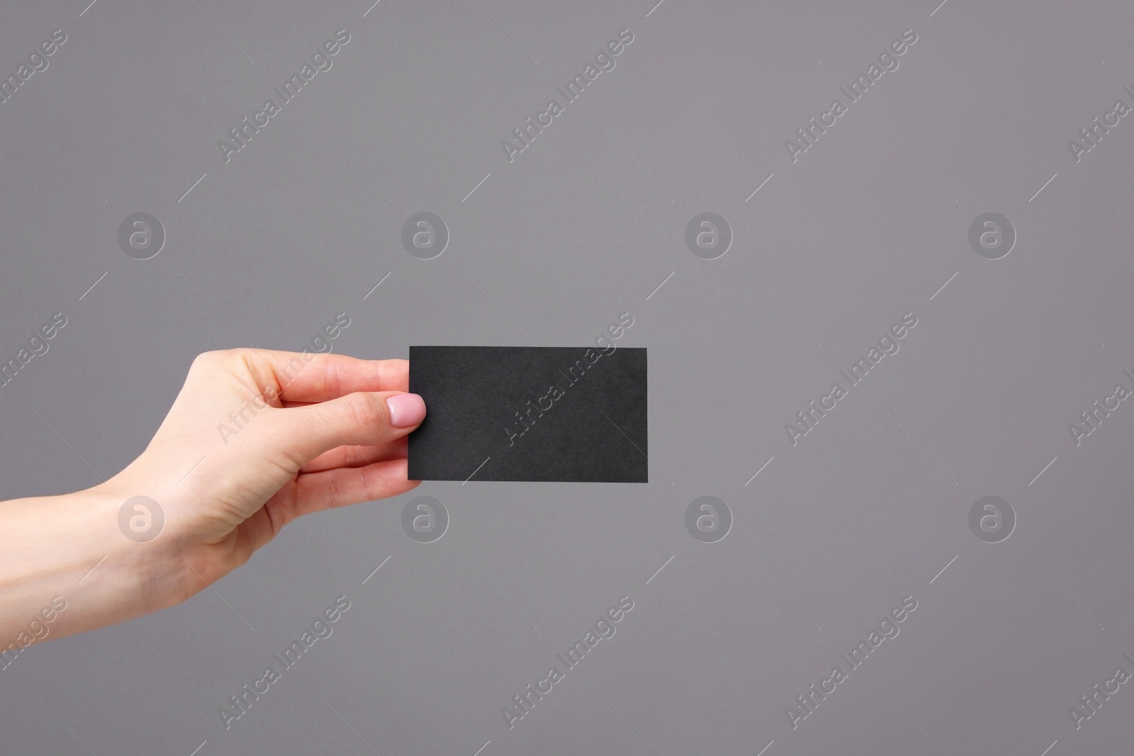 Photo of Woman holding blank business card on grey background, closeup. Space for text