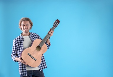 Young man with acoustic guitar on color background. Space for text