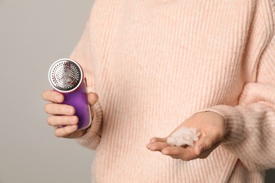 Woman in woolen sweater holding fabric shaver and lint on light grey background, closeup